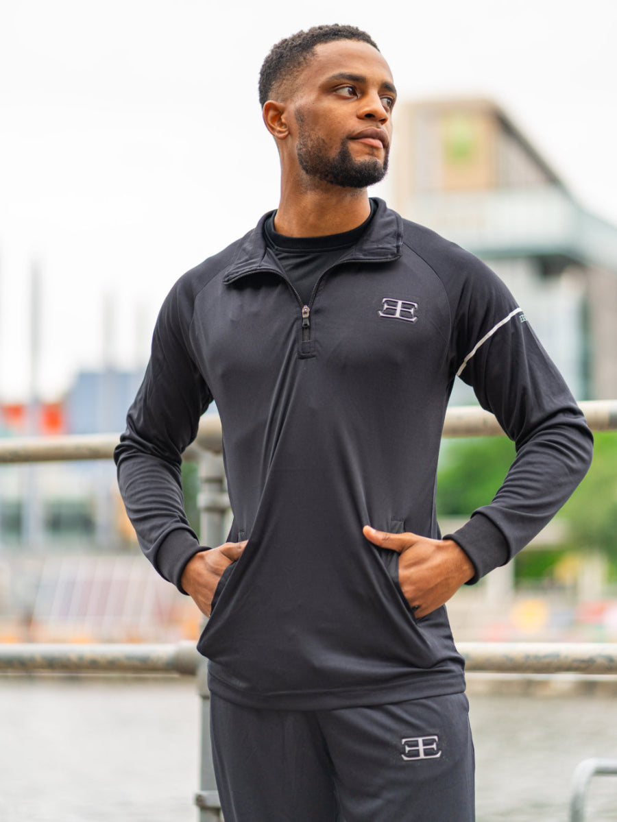 man wearing full black tracksuit set, black top and joggers with pockets. sporty look with brand logo showing