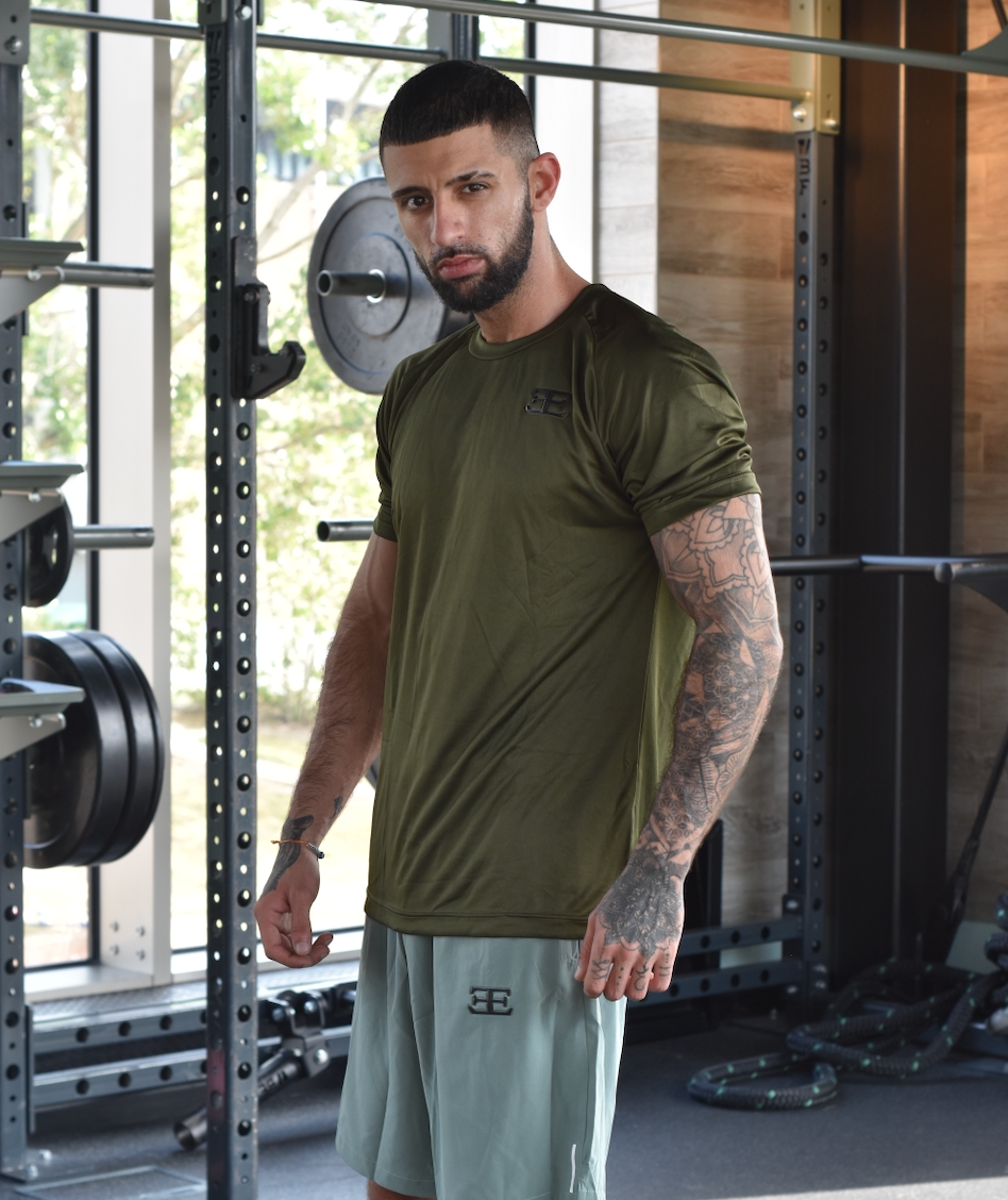 man wearing green gym clothing, shorts and tshirt with weights in the background