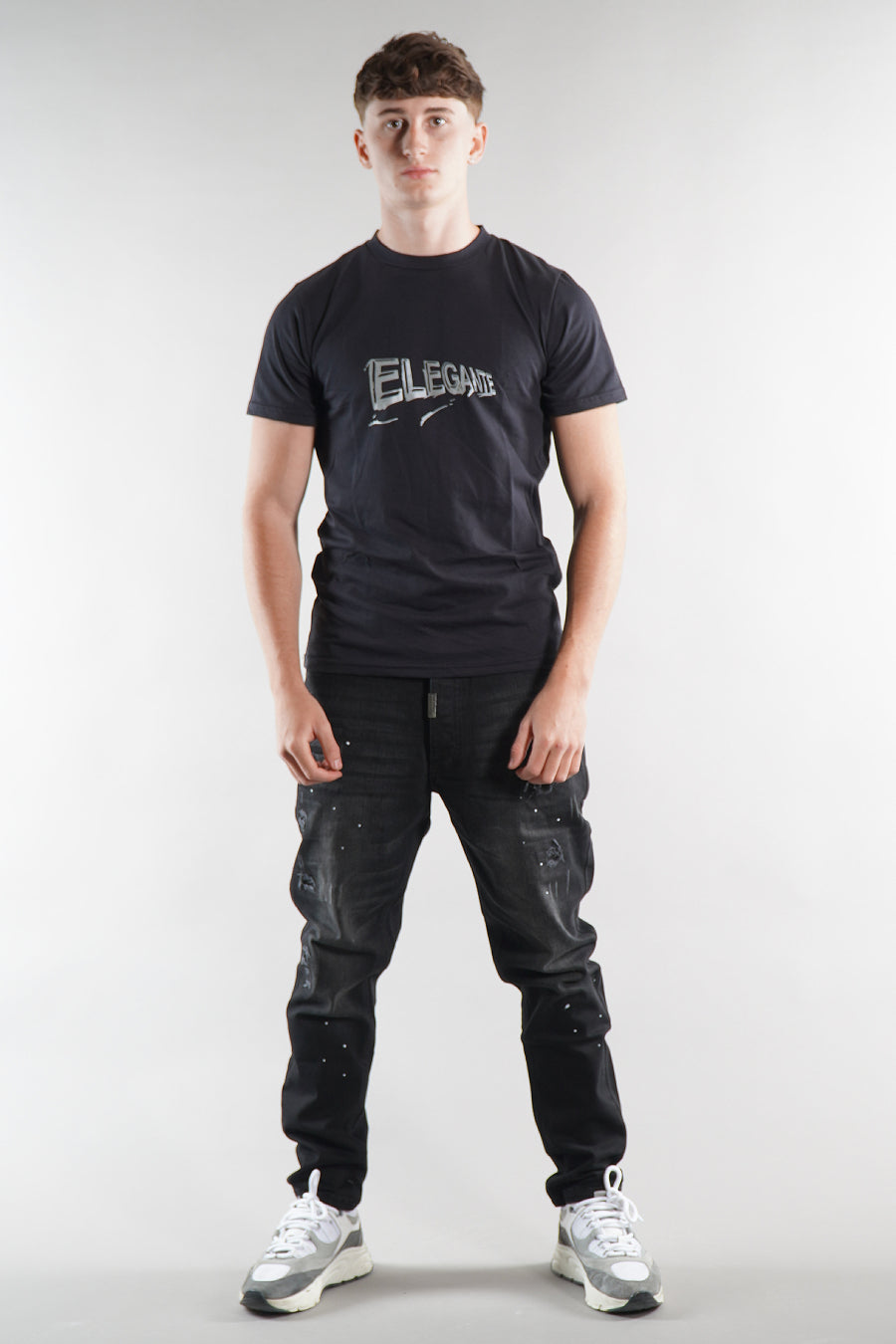 man wearing Elegante logo T-Shirt in black with black denim jeans on white background