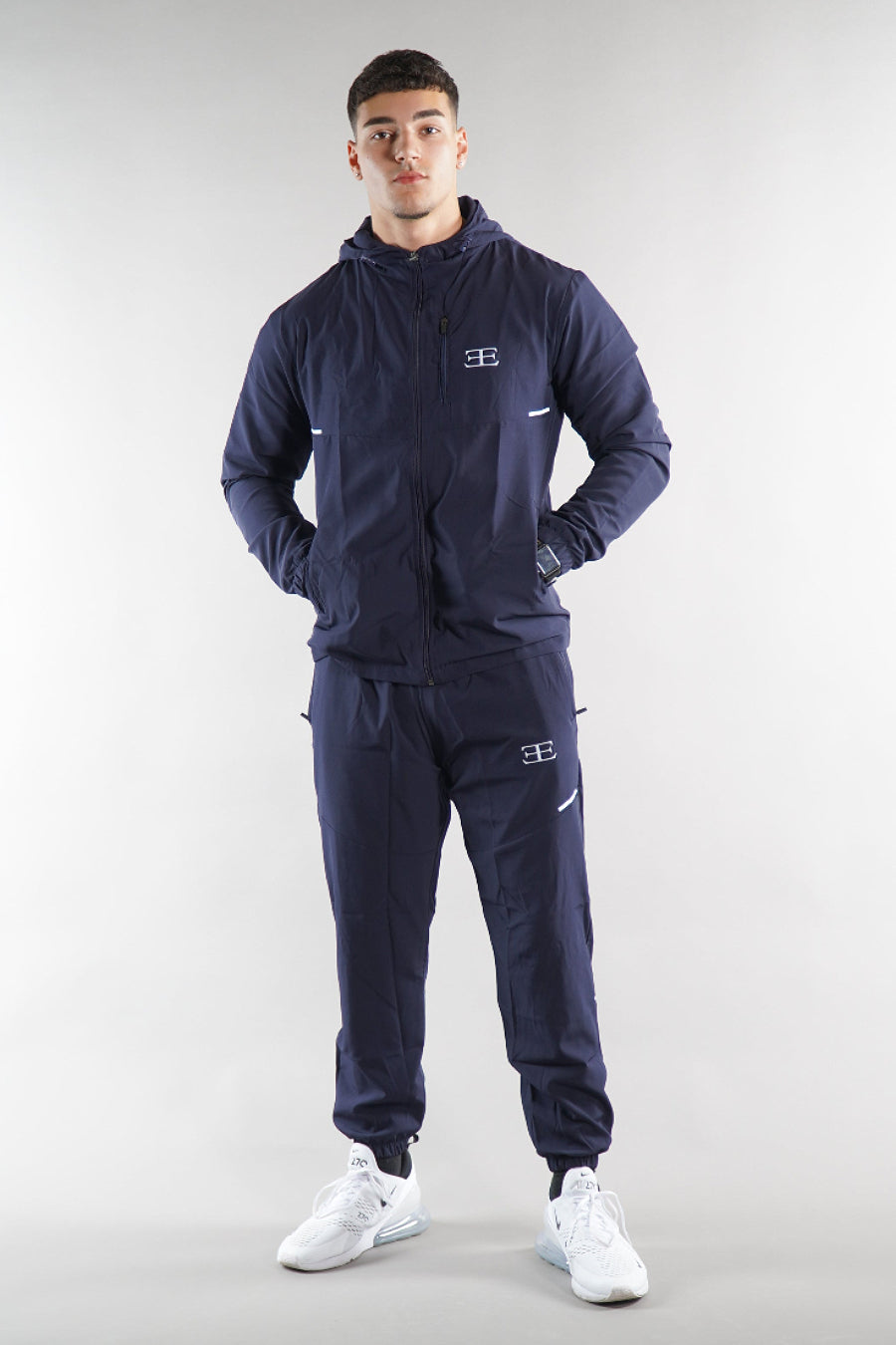man wearing navy tracksuit jacket and joggers on white background
