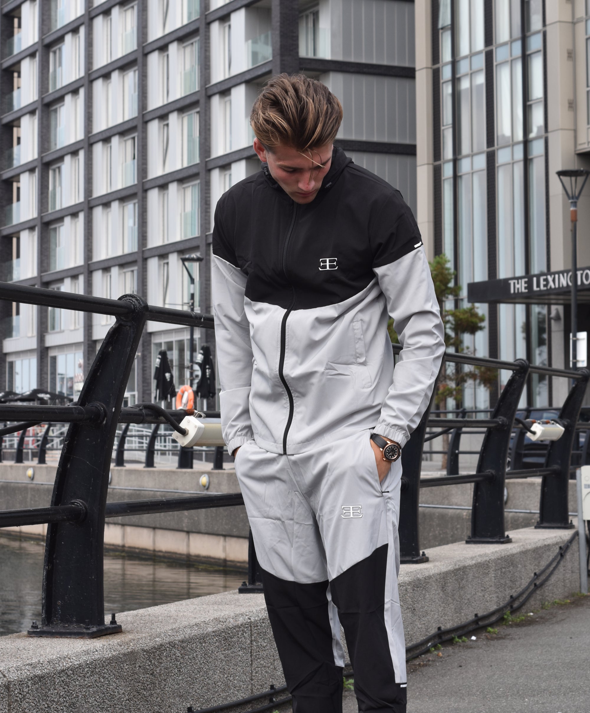 man wearing a black and white tracksuit with a brand logo, standing on a city street.