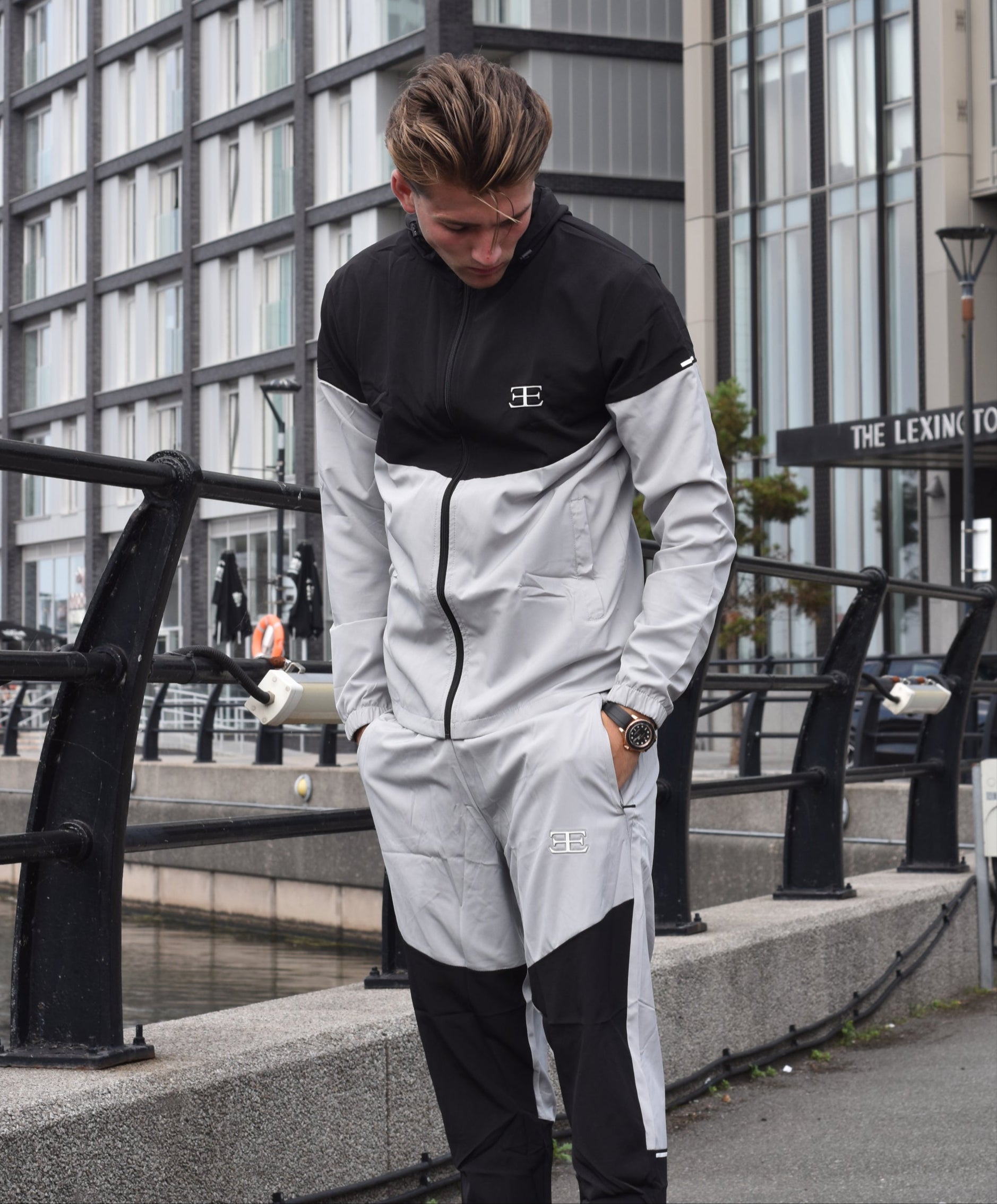 man wearing a black and white tracksuit with a brand logo, standing on a city street.