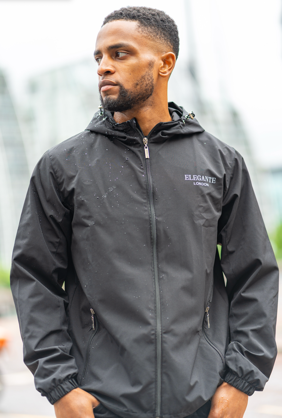 Man wearing a black waterproof raincoat with hood, with'Elegante' branding outdoor