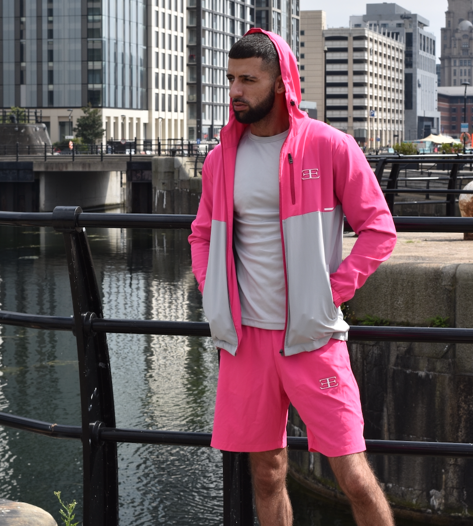 man wearing pink tracksuit jacket with hood and pink shorts with buildings in the background and