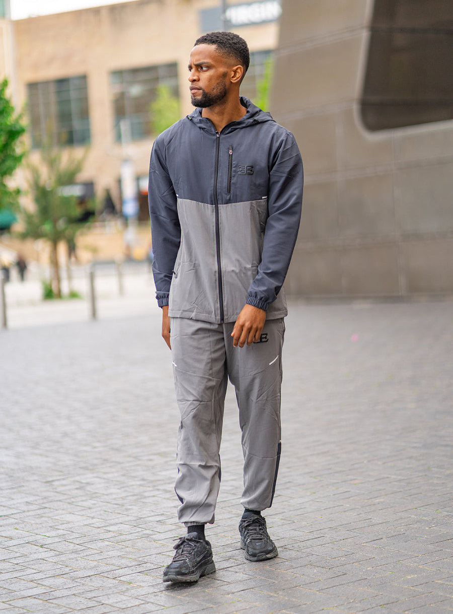 man wearing dark grey and light grey tracksuit with elegante logo on left chest, with buildings in the background