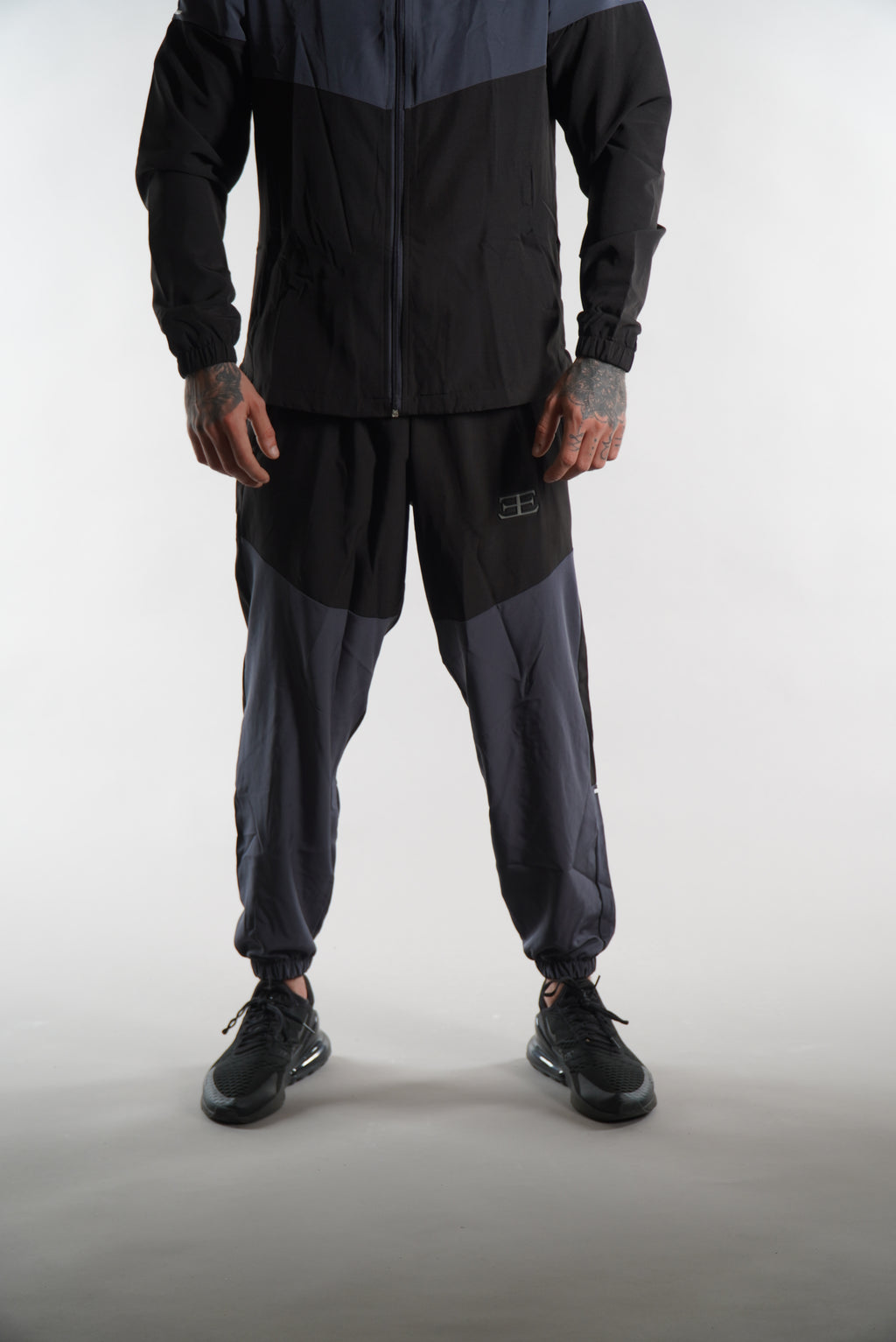 Man wearing black and dark grey tracksuit pants set, on white background, sports clothing for men
