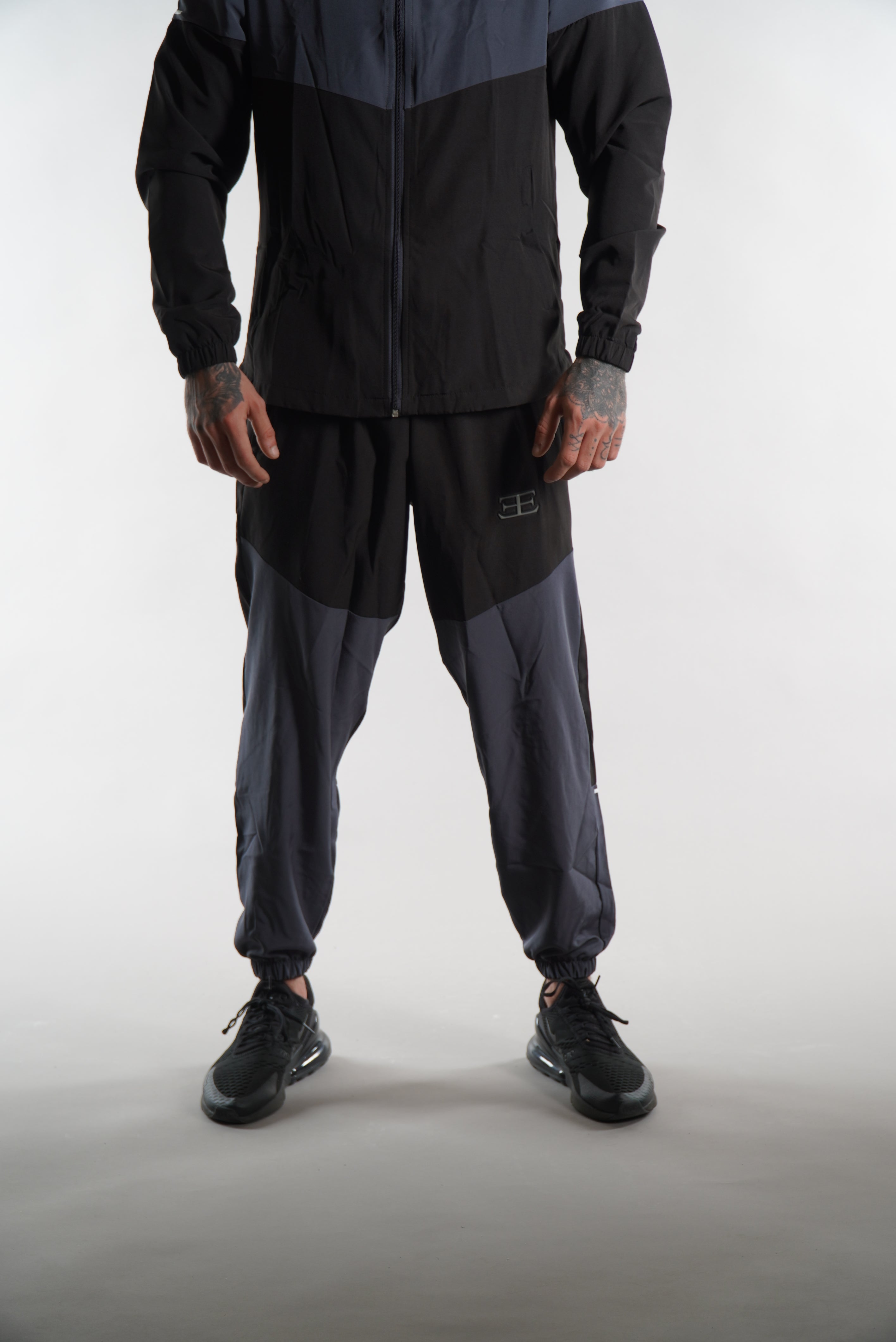 Man wearing black and dark grey tracksuit pants set, on white background, sports clothing for men