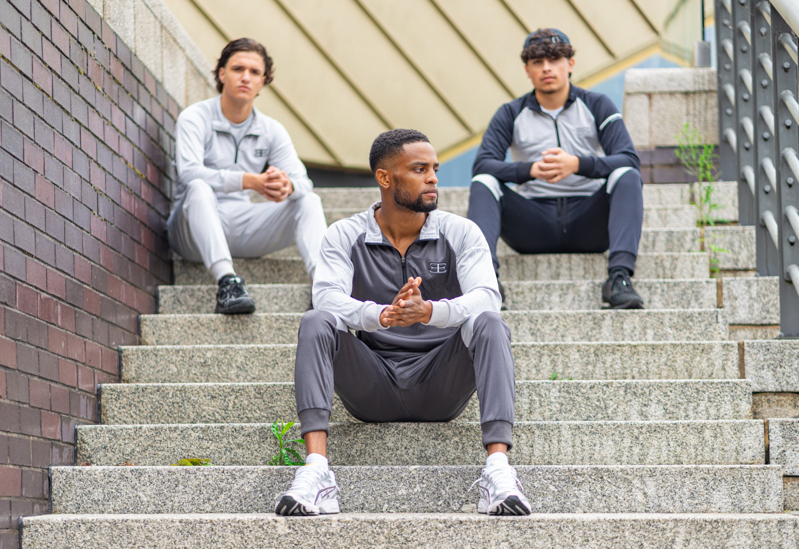 gymwear for men, sportwear, 3 sitting on steps men wearing zip tops and joggers in grey