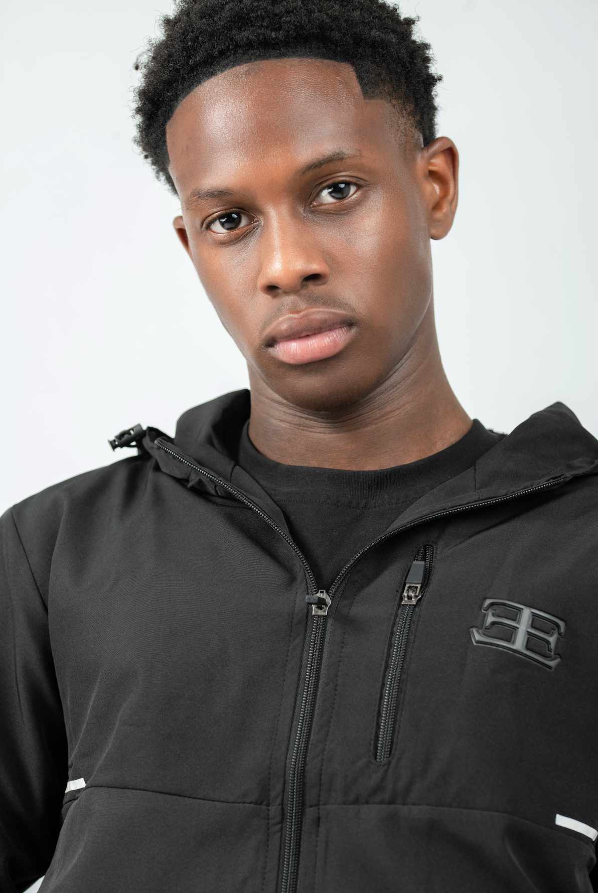 Man wearing a black jacket with a brand logo on a grey background