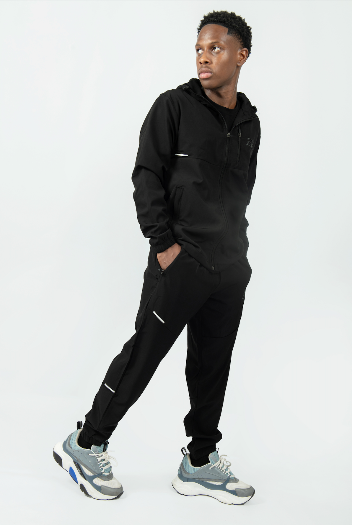 Person wearing a black tracksuit with gray sneakers on a white background