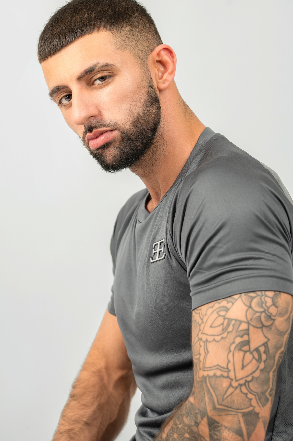 Man wearing a gray t-shirt with a logo on a plain background