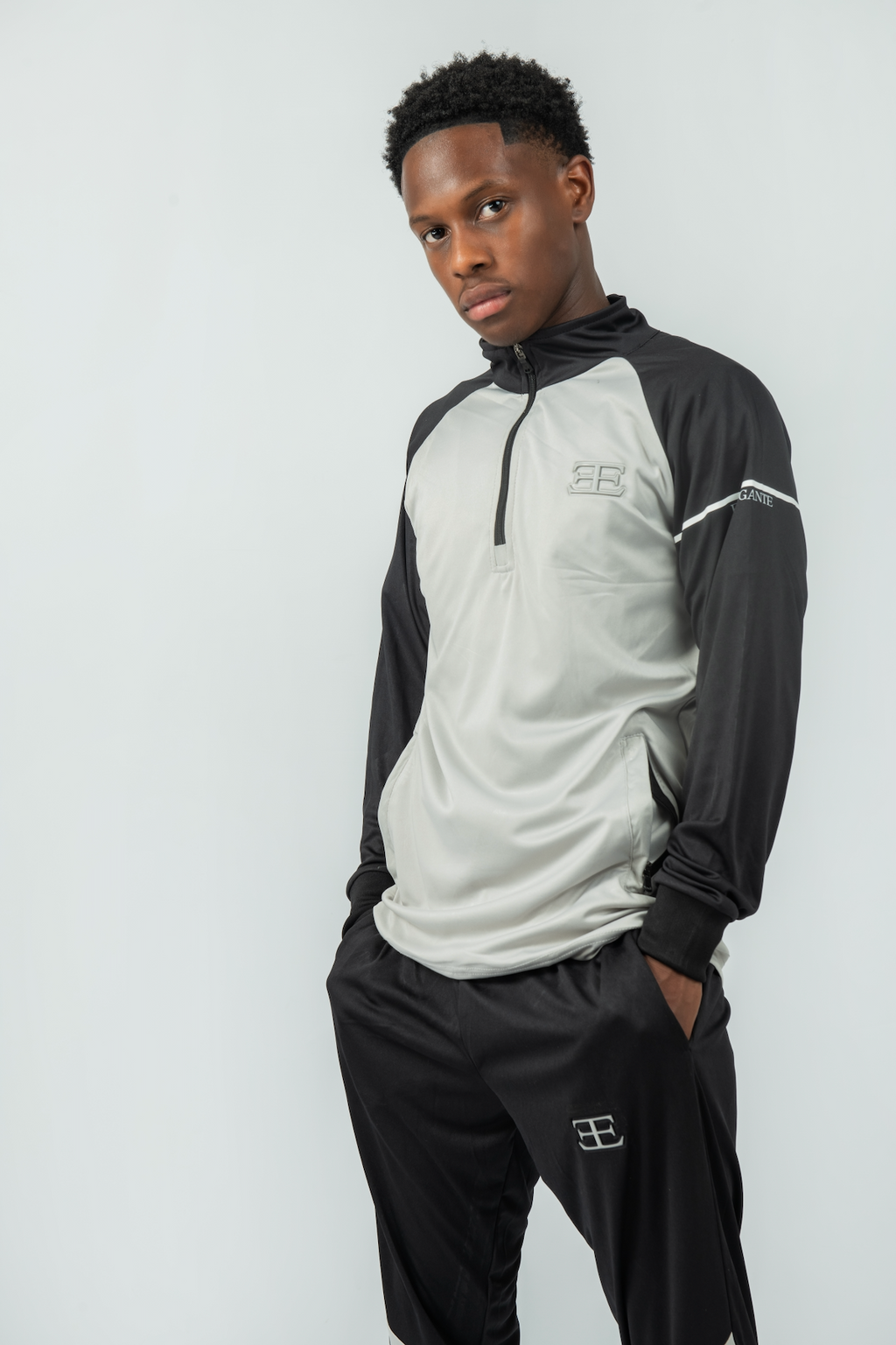 Person wearing a black and gray tracksuit with a logo on a white background