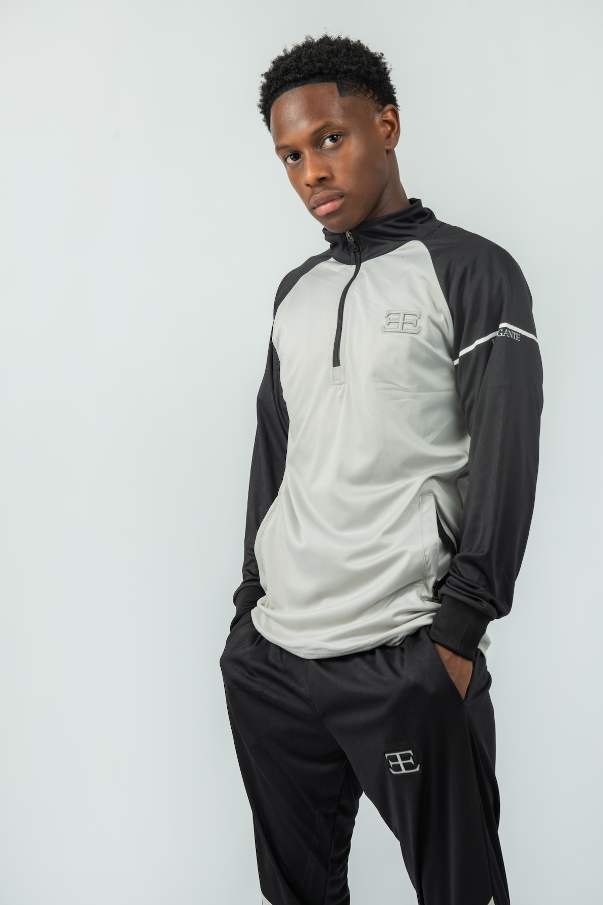 Person wearing a black and gray tracksuit with a logo on a white background