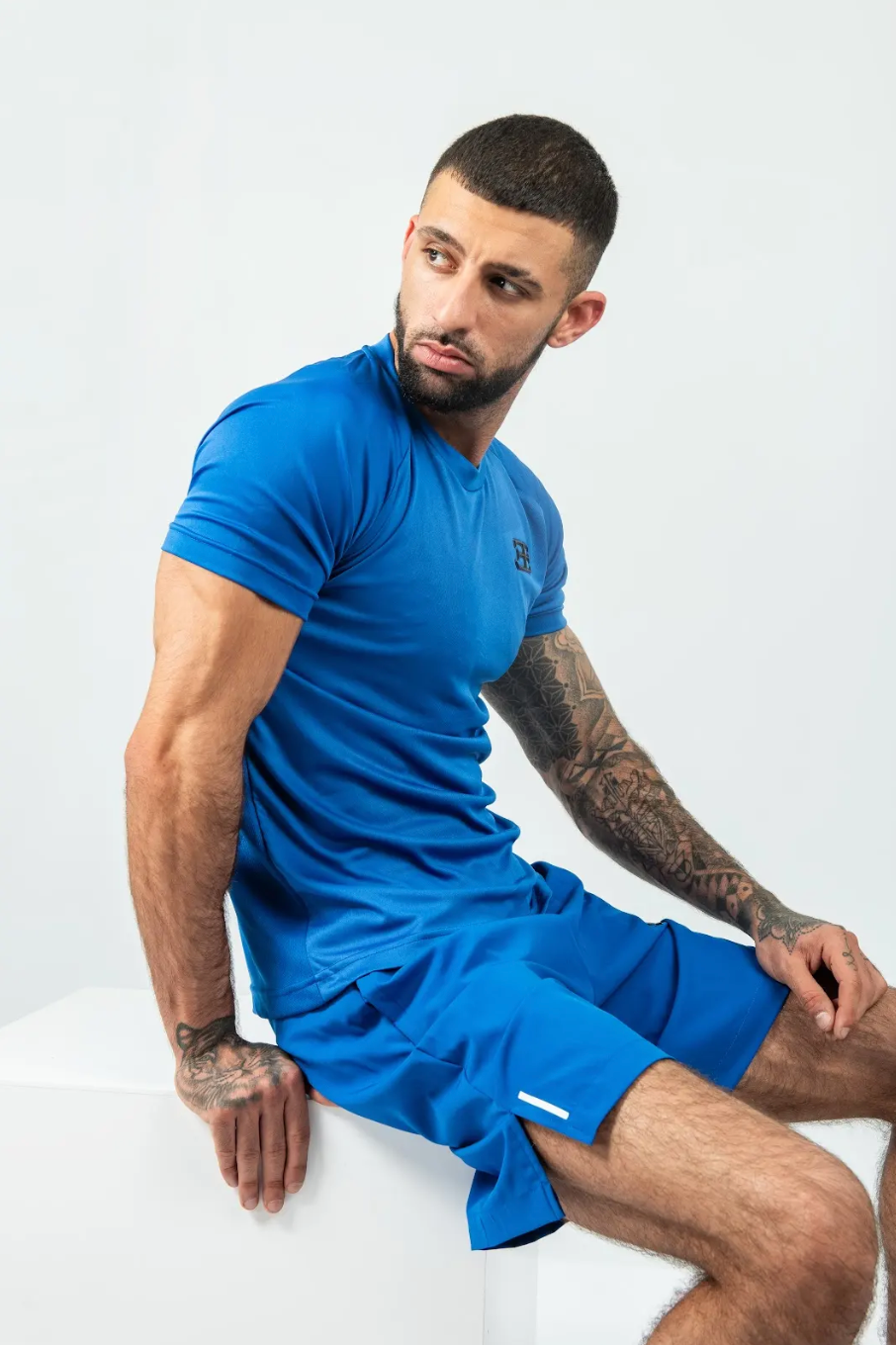Man wearing a blue athletic outfit sitting on a white surface with a plain background
