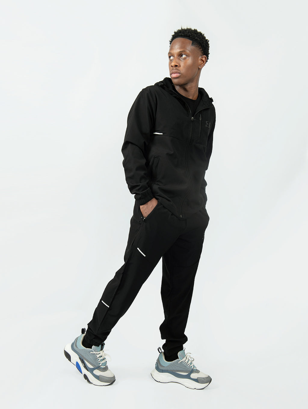 man wearing a black tracksuit with gray sneakers on a white background