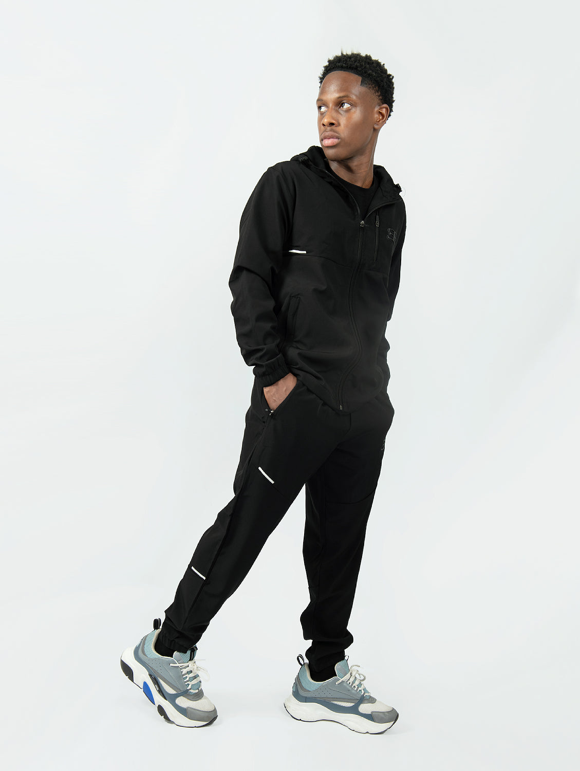man wearing a black tracksuit with gray sneakers on a white background