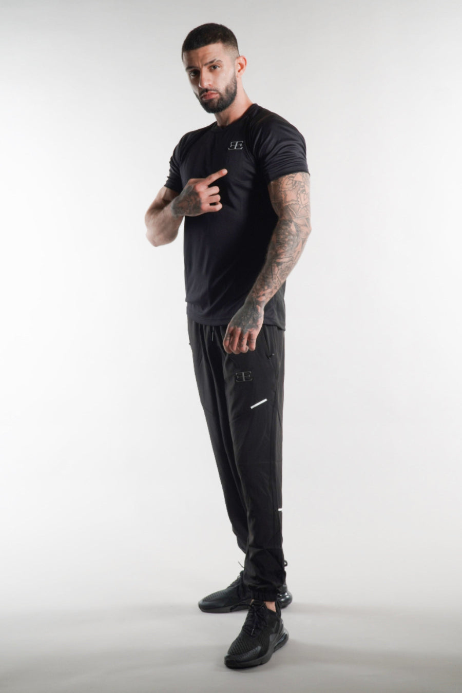 Man wearing a black t-shirt and tracksuit pants with elegante brand logo on a white background