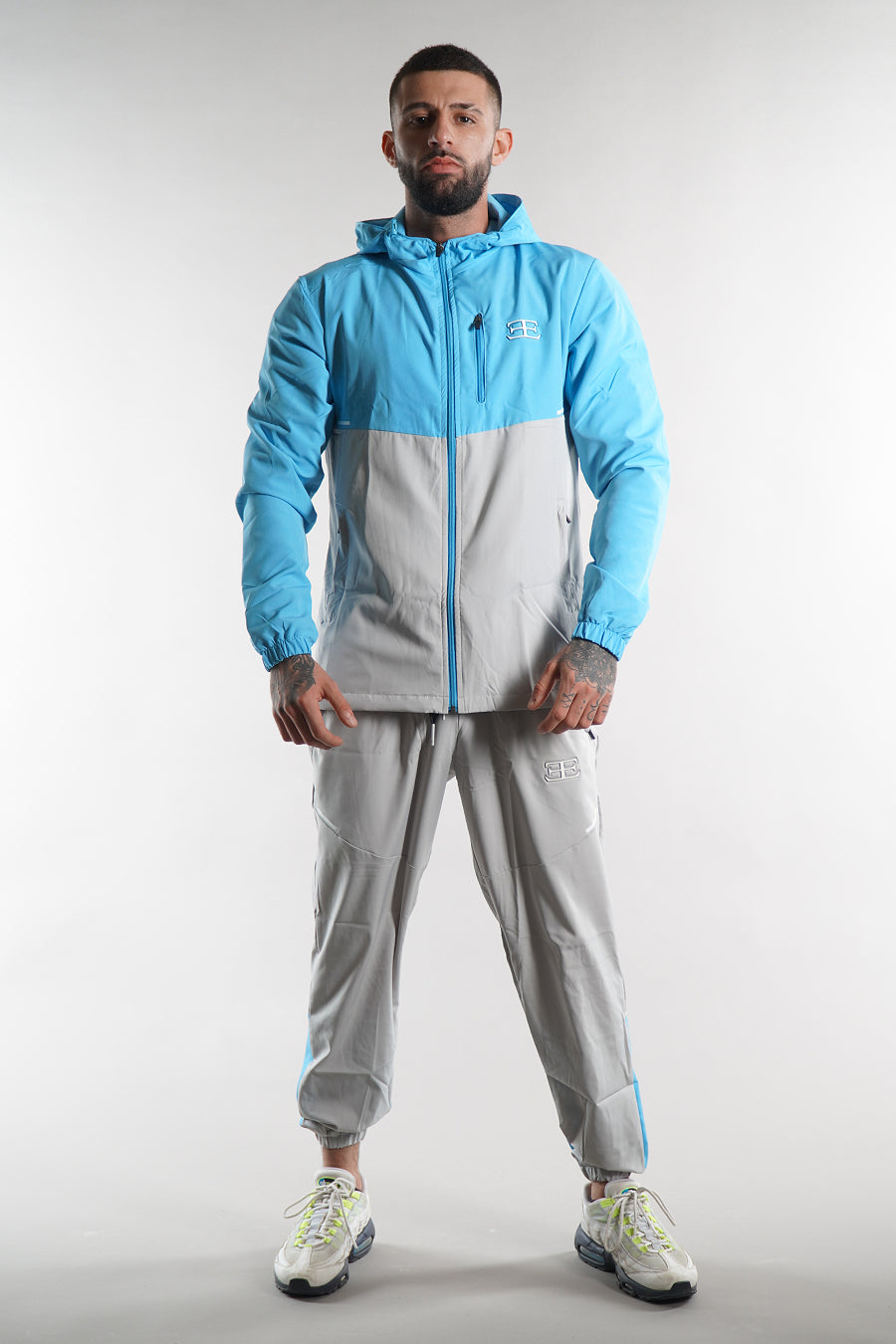 man wearing Elegante branded turquoise blue Tracksuit jacket with hood and grey blue joggers on white background