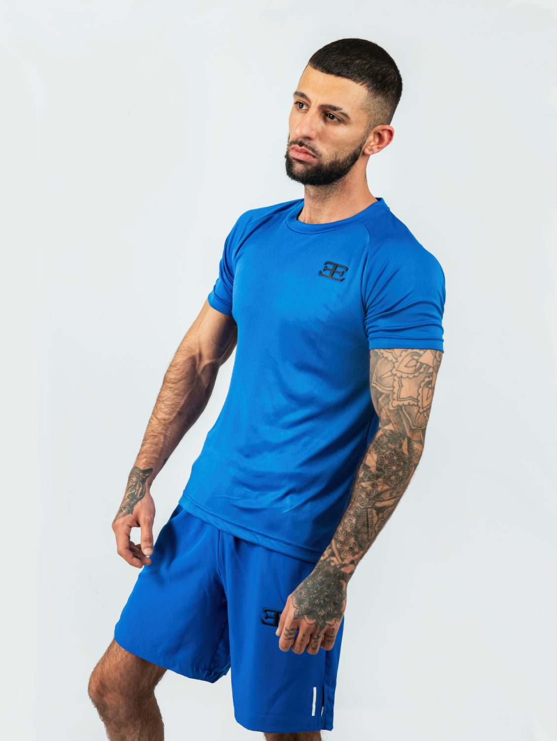 Man wearing a blue shorts and tshirt with elegante logo badge on chest and short posckets on a white background