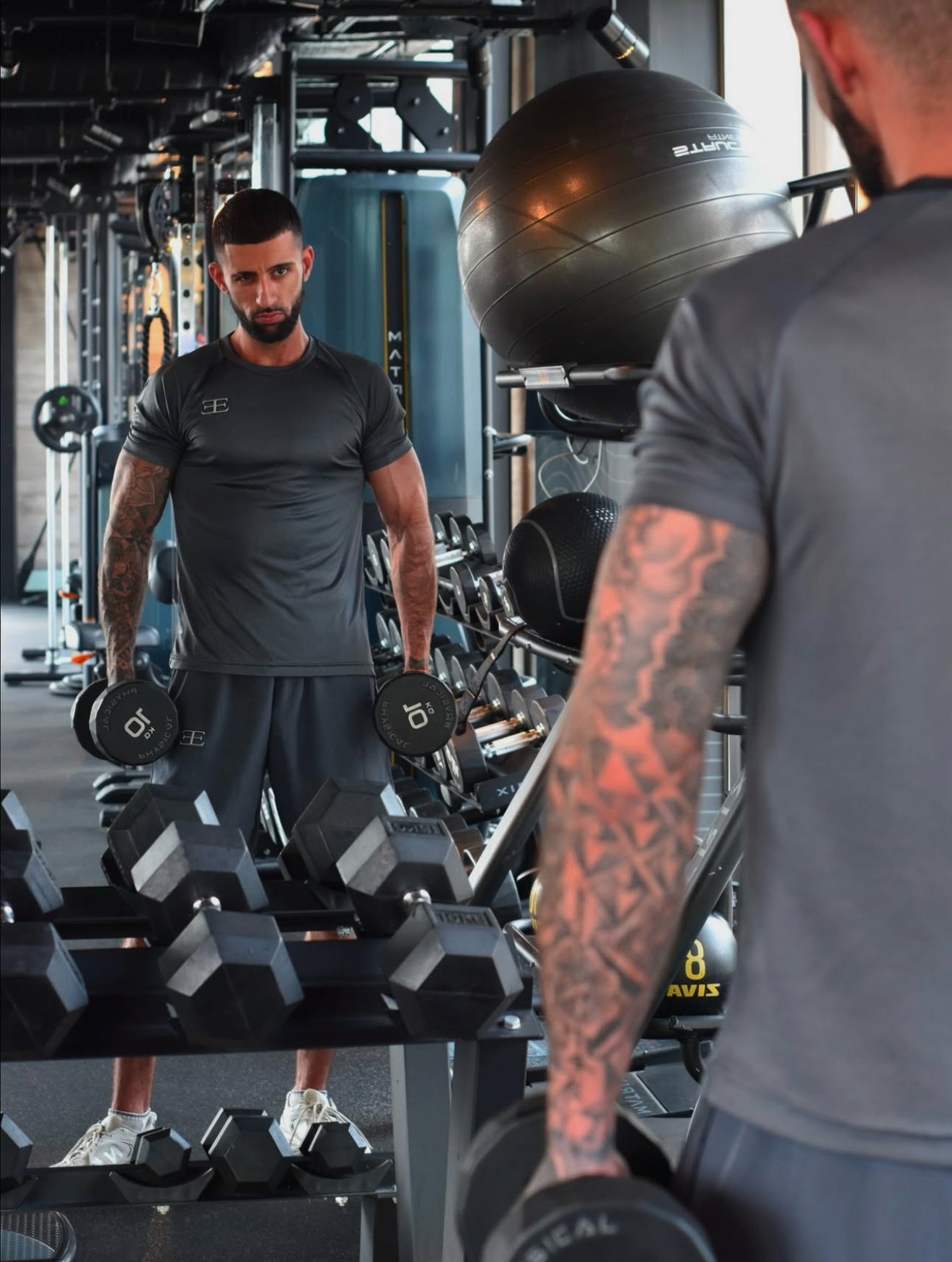 man in the gym lifting weights wearing elegante london clothing gym shorts and tshirt in grey, with elegante logo on chest