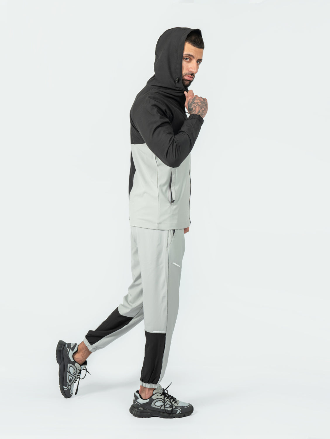 man wearing a black and gray tracksuit with the hood up, on a white background