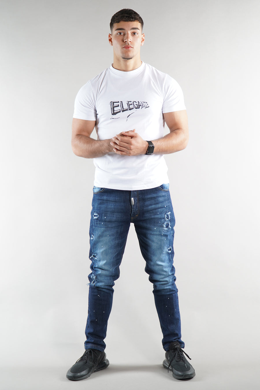 Man wearing a white t-shirt with text and blue designer jeans on a plain background
