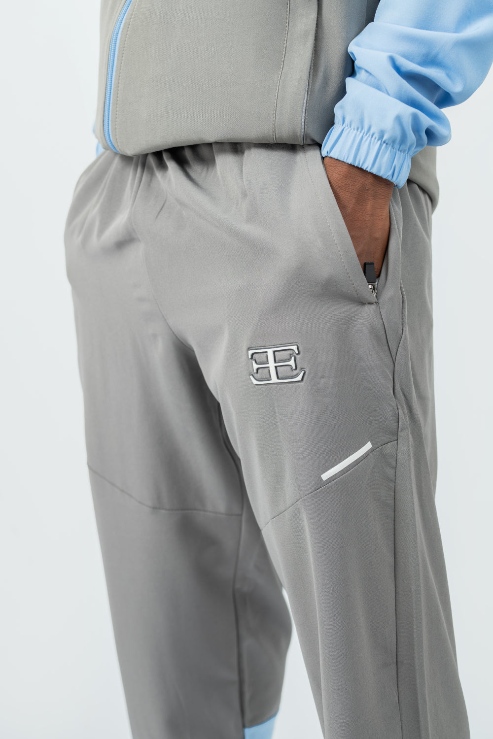 man with hand in tracksuit joggers pocket, tracksuit is grey with a logo on a white background