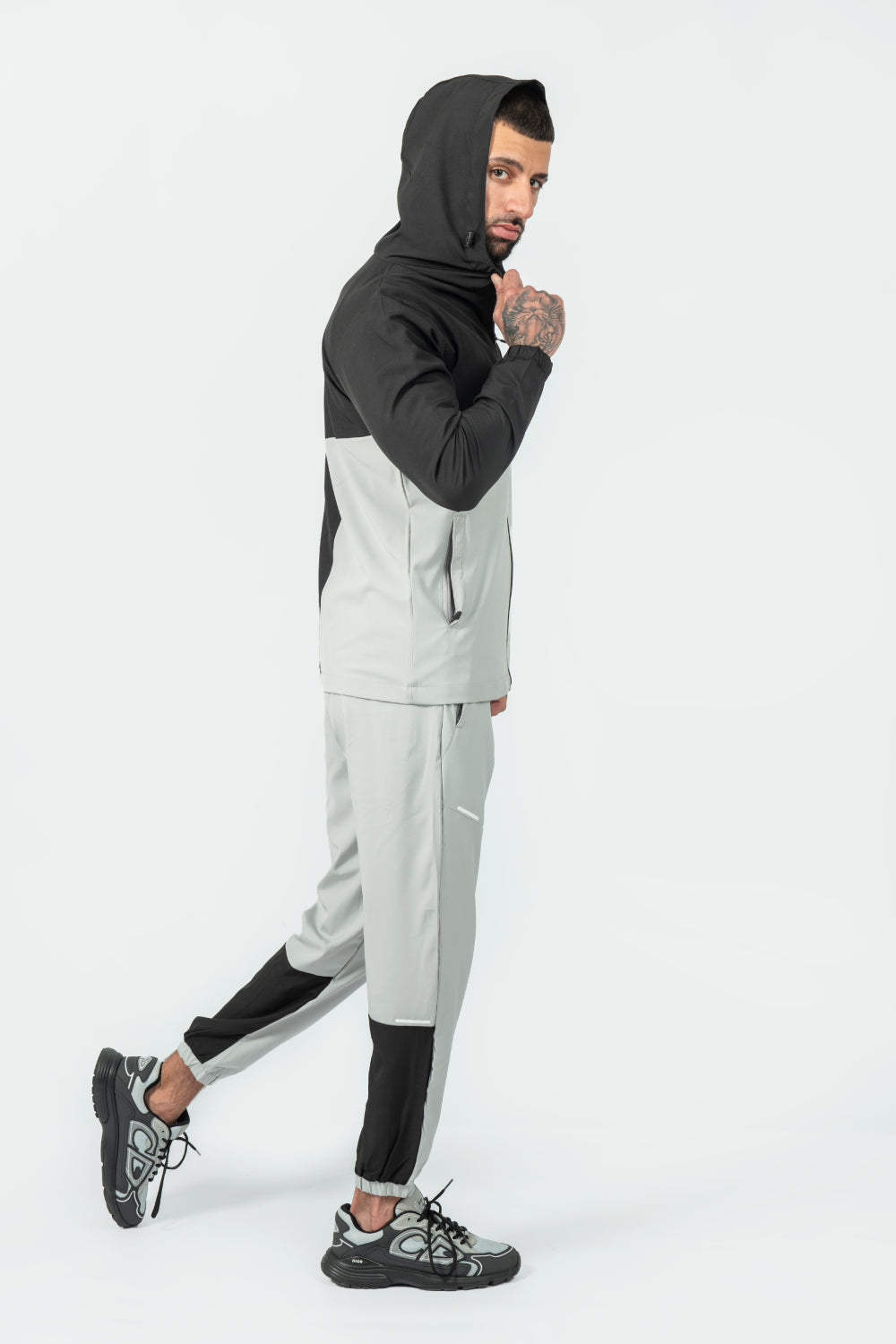 man wearing a black and gray tracksuit with hood up on a white background