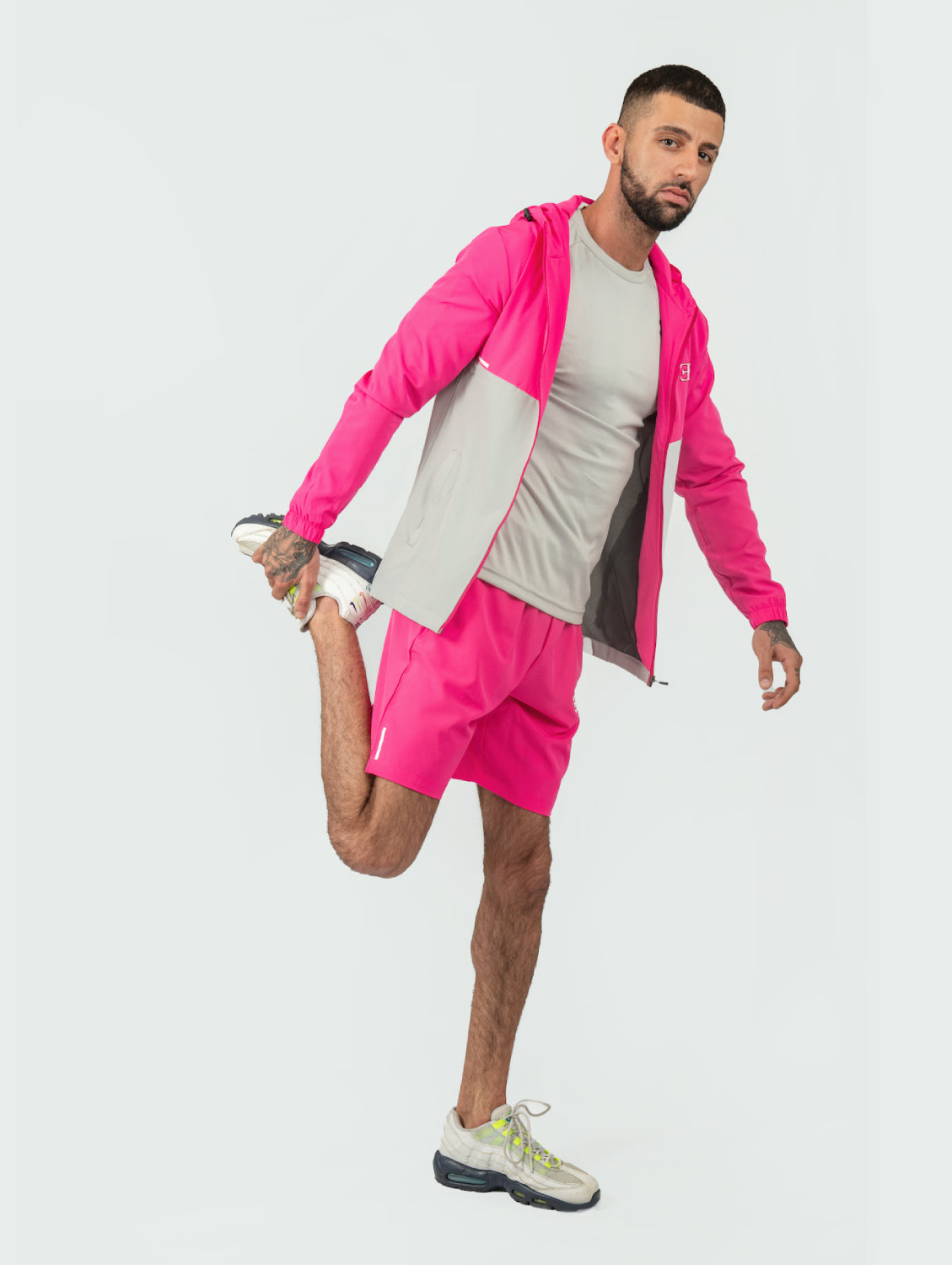 Man stretching in bright pink athletic jacket and shorts on a white background