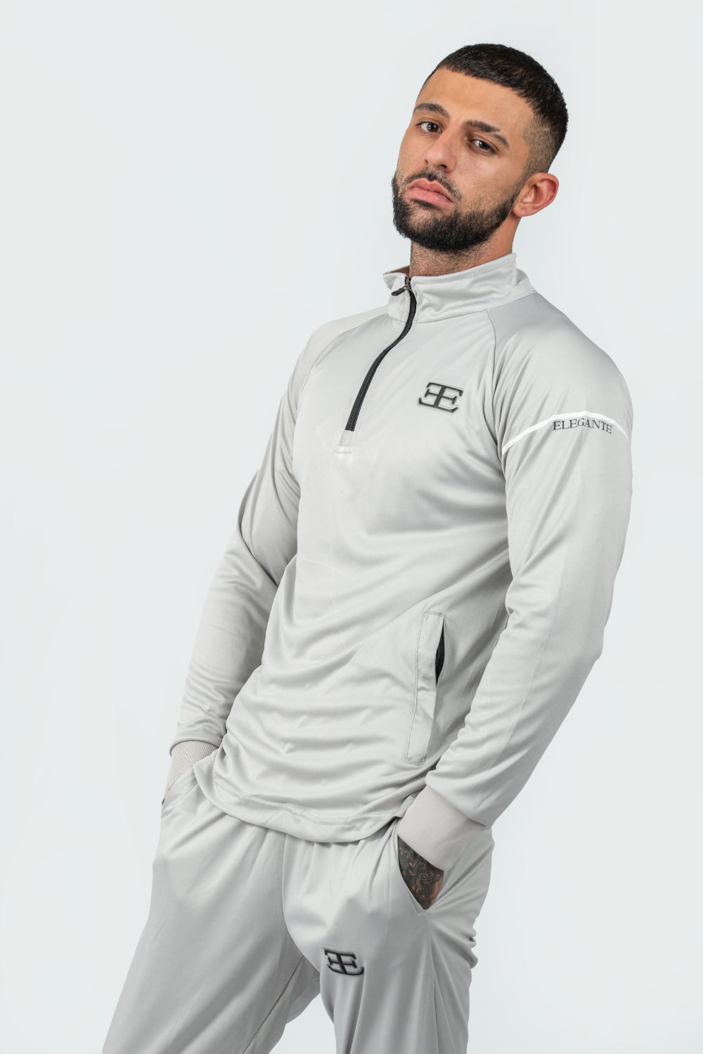 Man wearing a gray tracksuit with a brand logo on a white background