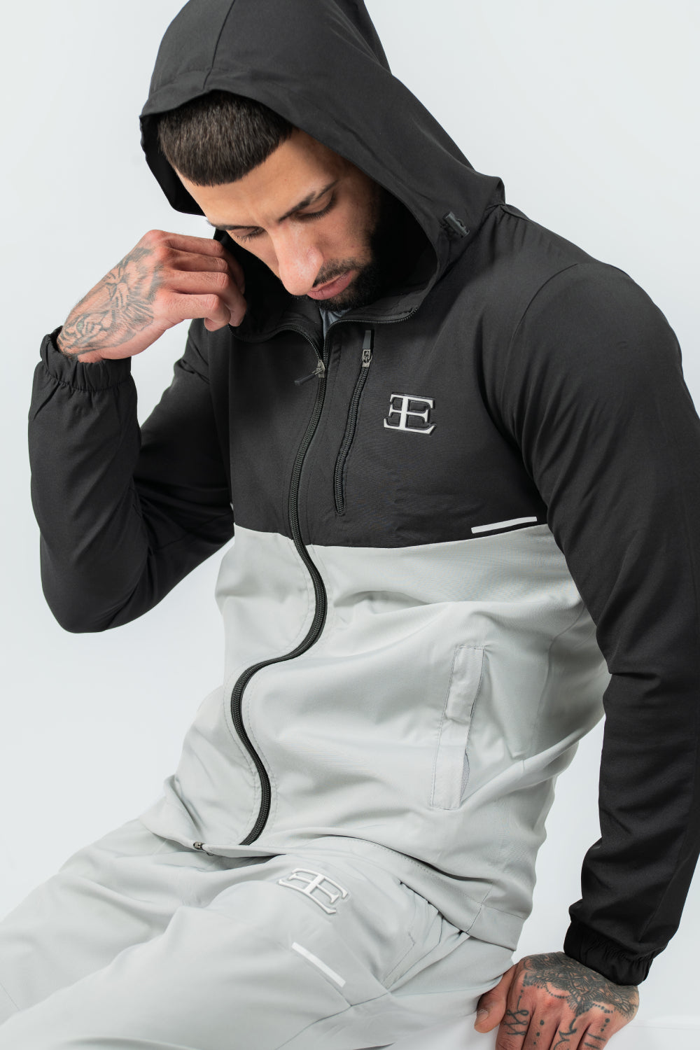 Person wearing a black and gray tracksuit with a brand logo on a light gray background