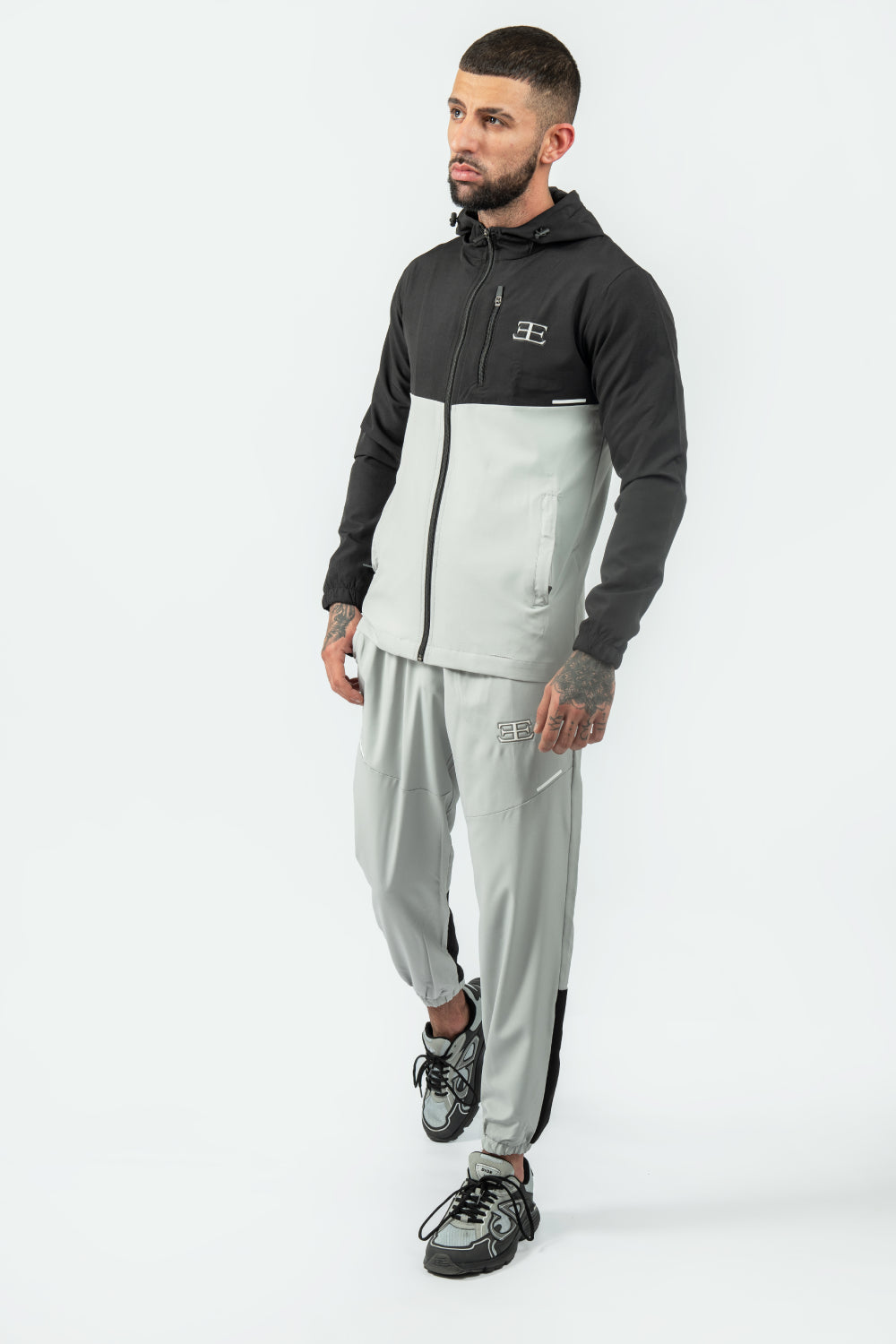 Man wearing a black and gray tracksuit with a logo on a white background
