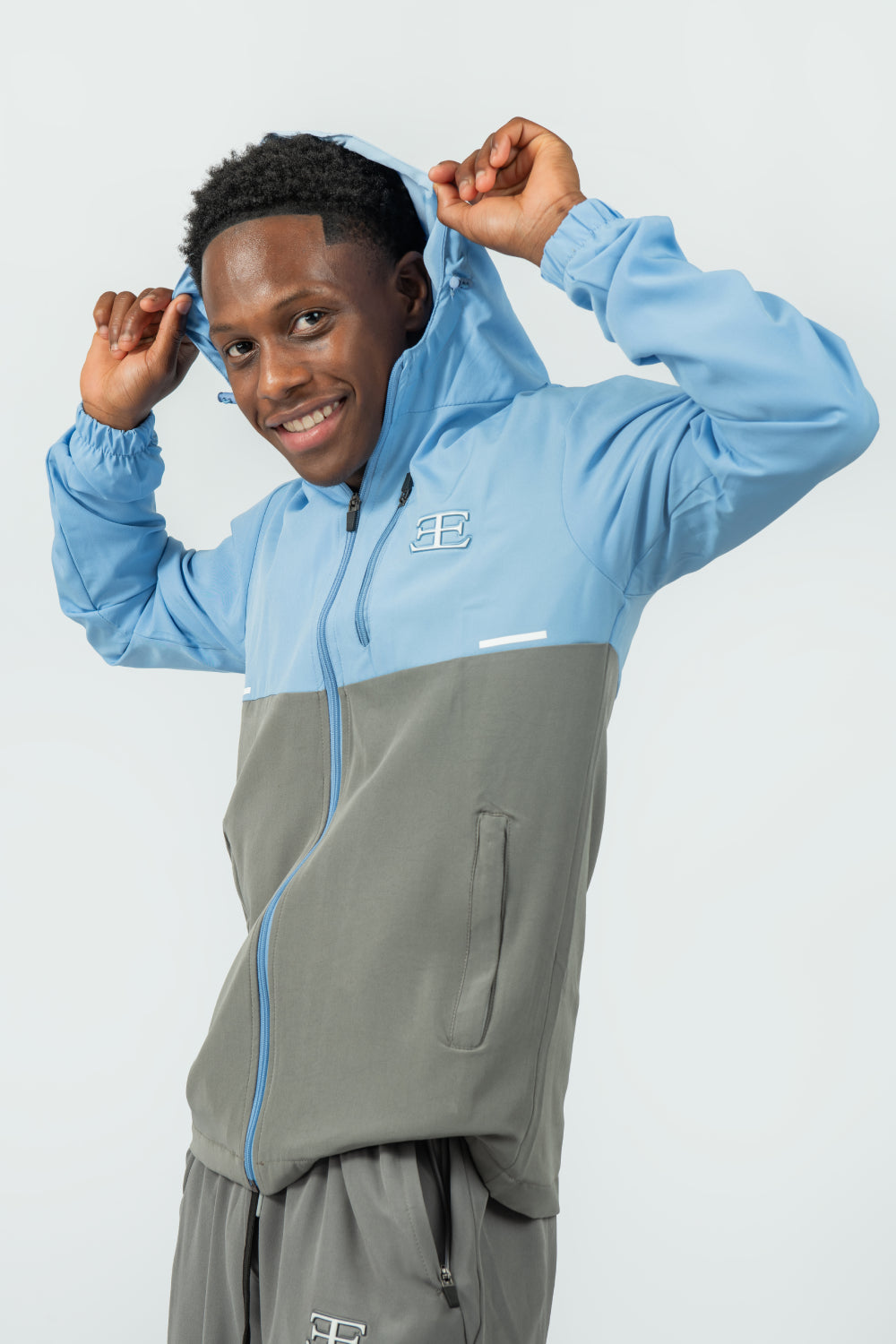 man wearing a two-tone blue and grey jacket with a logo and hood on a light grey background