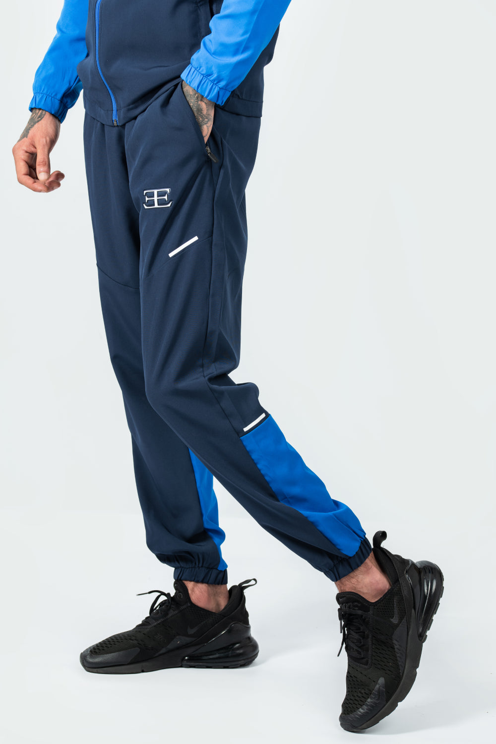 man wearing navy and blue tracksuit with black shoes on a white background