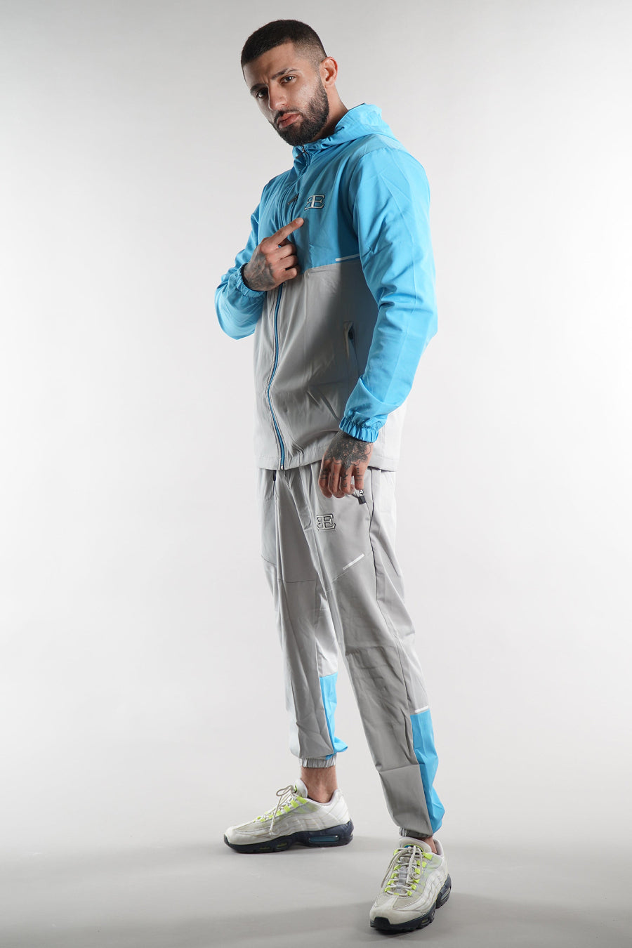 man wearing Elegante branded turquoise blue Tracksuit jacket with hood and grey blue joggers on white background